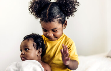Portrait of cute adorable little african american baby and sister girl playing in a white bedroom