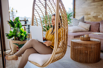 Work from home or study online, concept with woman working at laptop outdoor on terrace, sitting in hanging chair.