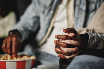 Selective focsu shot of unrecognizable Black man and Caucasian woman in love watching movie at cinema holding hands