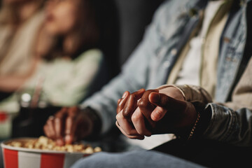 Selective focus of unrecognizable ethnically diverse couple holding hands while watching film at...