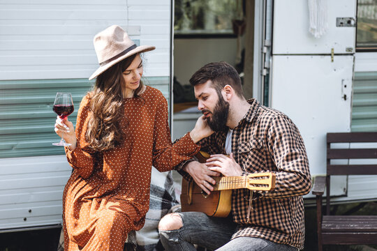 Young beautiful loving couple travelling across country in the van. Millennial man and woman in a travel camper. Cozy atmosphere, vacations vibe. Drinking tea, playing guitar