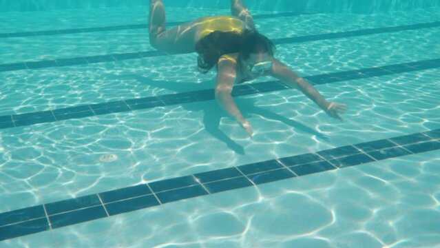 The camera goes down under, there's a girl in a yellow swimsuit and a mask. Swimming pool and camera under water. Slow motion