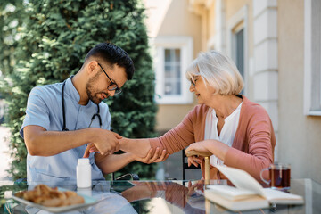 Male nurse examining arm of senior woman on nursing home patio.