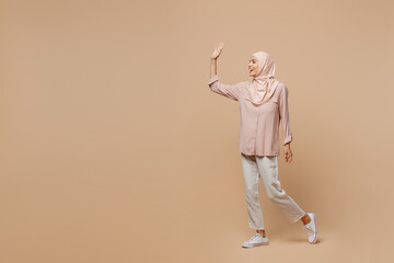 Fototapeta na wymiar Full size young arabian asian muslim woman she wear abaya hijab pink clothes walking going waving hand isolated on plain pastel light beige background People uae middle eastern islam religious concept