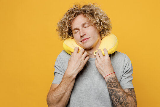 Traveler tourist calm man he 20s wear grey t-shirt sleep with neck pillow close eyes isolated on plain yellow background studio. Passenger travel abroad on weekends getaway Air flight journey concept