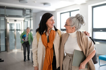 Happy mature woman student with book discussing with teacher in corridor in university.