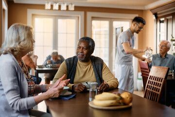 African American senior man and his female friend talk at dining table in nursing home.