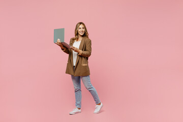 Full body young successful employee business woman 30s she wear casual classic jacket hold use work on laptop pc computer look aside on workspace area isolated on plain pastel light pink background.