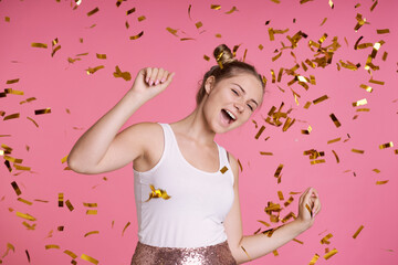 Caucasian teenage girl on pink background dancing among golden confetti