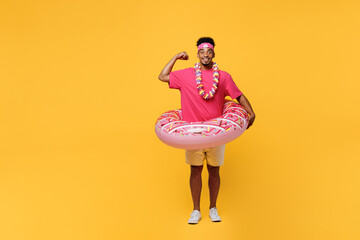 Full body surprised happy strong young man 20s he wearing pink t-shirt inflatable rubber donut ring show muscles near hotel pool isolated on plain yellow background. Summer vacation sea rest concept.