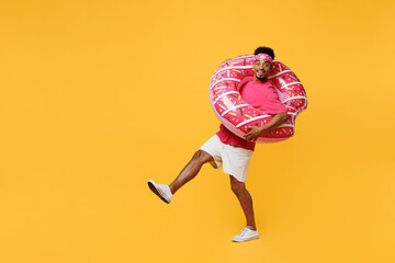 Full body side view young man he wear pink t-shirt bandana near hotel pool hold inflatable rubber ring raise up leg leaning back isolated on plain yellow background. Summer vacation sea rest concept.