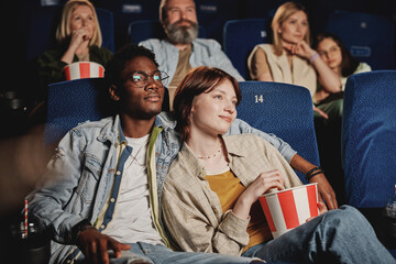 Stylish young gen Z Black man hugging his Caucasian girlfriend while watching movie together at cinema - obrazy, fototapety, plakaty