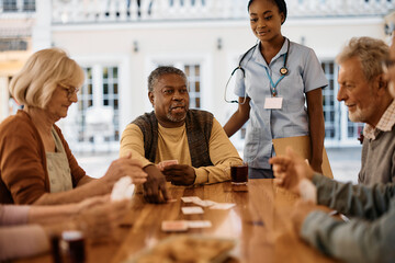 Multiracial group of senior friends play cards in nursing home.