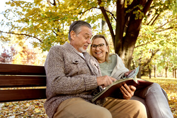 Senior couple sitting at the bench in park and looking at old photos