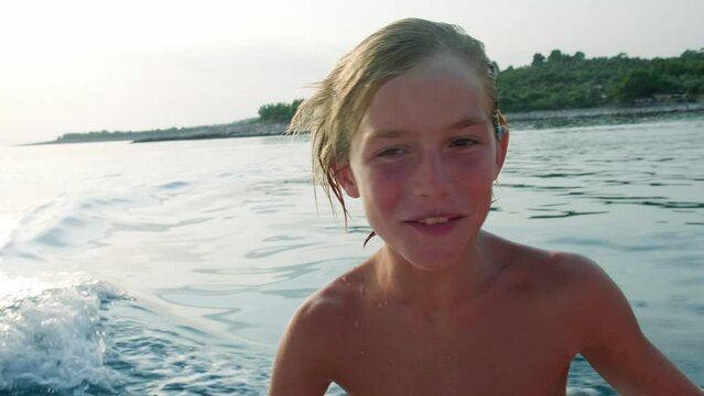 Close up portrait of happy kid riding a boat in the sea during summer vacation, authentic laughter and emotion.