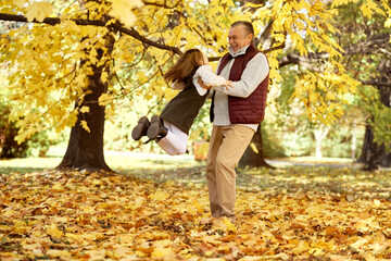 Senior man with her granddaughter have fun at the park in autumn