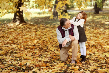 Senior man with little girl playing at the park in autumn