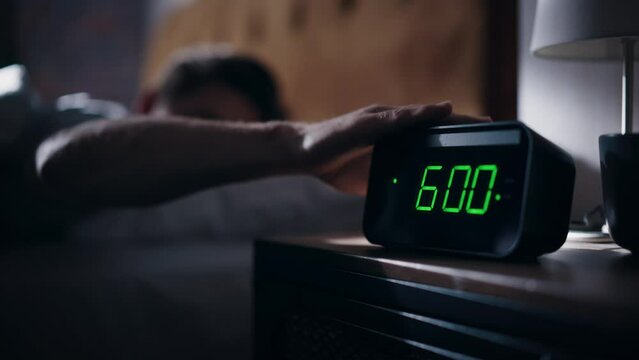 Man Wakes Up, Turns off Alarm Clock with Frustration. Early Rising Productive Man Ready Start a Day full of New Problems. Focus on the Clock Showing Six A.M. Bedside Nightstand bedroom Apartment