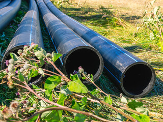 Large diameter plastic pipes for outdoor water supply. HDPE pipes lie in the field. Smooth black...