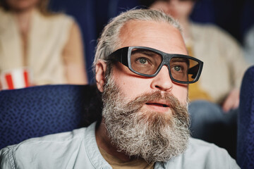 Close-up portrait of mature Caucasian man with beard on face wearing polarized 3D glasses watching...
