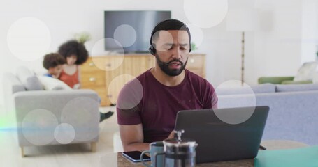 Animation of dots moving over happy biracial man working on laptop at home