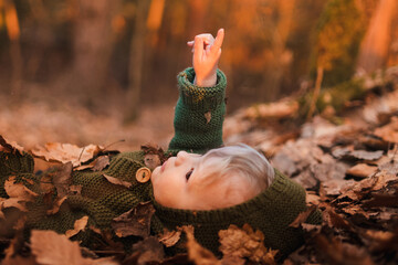 Little boy lying in dry leaves in nature, autumn concept
