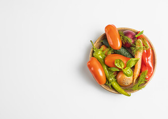 Wooden plate with fresh vegetables: green pepper, tomato, onion, carrot, cucumber, basil, dill on white background, top view, rustic concept