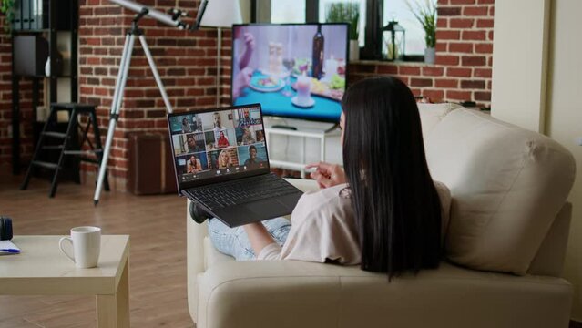 Woman working remotely from home while in online meeting videocall on laptop sitting on sofa in apartment. Freelancer working from home while discussing with coworkers on internet conference.