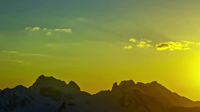 The rugged snowy peaks of the European Alps mountain range during a bright sunset - time lapse