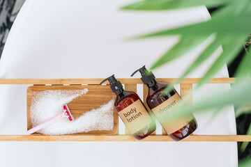 bottles with bodycare cosmetics products on bamboo tray on bathtub in bathroom
