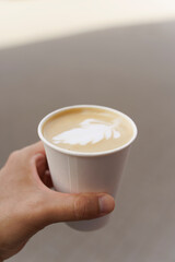 Paper cup of cappuccino coffee in hand on city street. Takeaway coffee drink