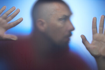 A man with fear on his face touching translucent glass surface with his hands, mystic concept.