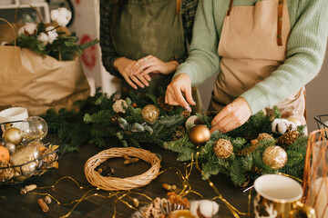 Two millennial women making Christmas wreath using pine branches and festive decorations. Small business - obrazy, fototapety, plakaty