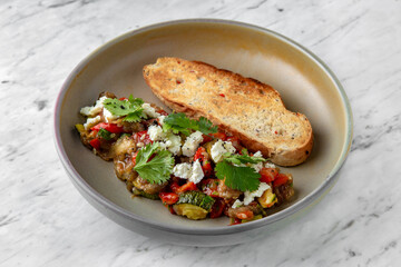 Soaked vegetables: eggplant, tomato, zucchini with ruddy toast in a  plate on a marble background. Restaurant banquet menu.
