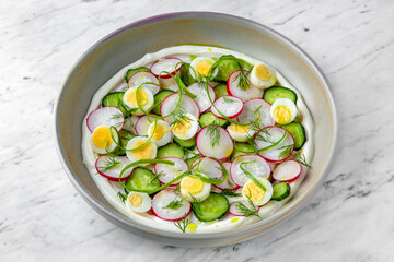 Fototapeta na wymiar Salad of quail eggs, radishes, cucumbers and yogurt in a plate on a marble background. Restaurant banquet menu.