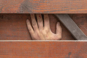 A creepy person's hand is trapped between boards and metalwork, an accident at work.