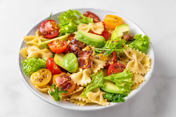 Pasta farfalle salad with tomato, bacon, avocado and mustard dressing in a plate on white table. Close up