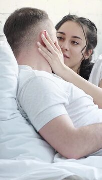 vertical video of happy brunette woman touching face of boyfriend while lying on bed