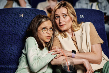Caucasian woman and her preteen daughter feeling scared when watching horror movie at cinema