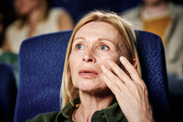 Close-up portrait of mature Caucasian woman getting emotional when watching drama movie at cinema