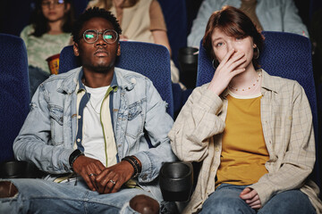 Young Black man and his Caucasian female friend watching sad drama movie in cinema, young woman...