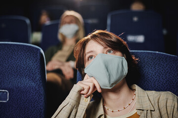 Unrecognizable young Caucasian woman wearing protective mask watching movie at cinema, quarantine...