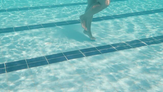 The girl's legs are under water, she jumps. Swimming pool and camera under water. Slow motion