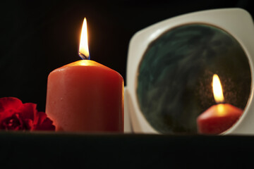 a red rose and a burning red candle with a reflection in the mirror on a black background in Gothic style