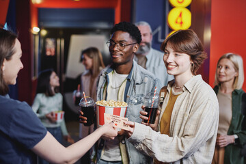 Joyful young Black man and Caucasian woman passing their tickets for movie to cinema hall worker
