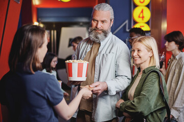 Modern mature couple passing their tickets for movie to young female cinema hall worker