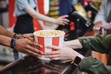 Unrecognizable food court worker giving bucket of popcorn to customer, selective focus shot