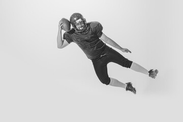 One american football player wearing retro stlye sports uniform in action and motion isolated on white background. Monochrome