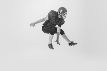 Studio shot of american football player jumping isolated on white background. Concept of sport, achievements, retro style. Monochrome