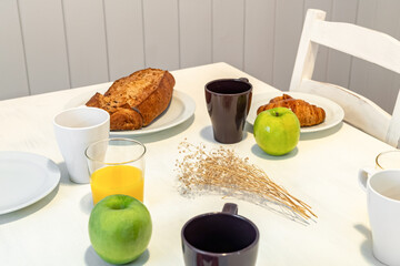 Fresh tasty breakfast served on a white table with croissants, apples and orange juice.